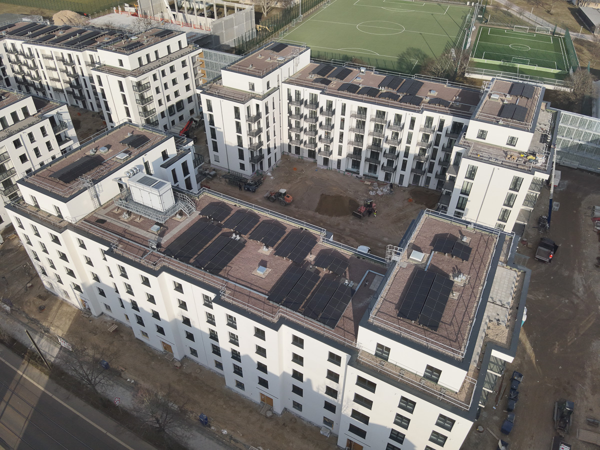 Neubau-Wohnquartiers mit installierter Photovoltaikanlage auf den Flachdächern der Mehrfamilienhäuser. Das Projekt zeigt die professionelle Umsetzung einer großflächigen PV-Anlage zur nachhaltigen Stromerzeugung im urbanen Wohnungsbau. Die Solarmodule wurden auf mehreren Gebäuden montiert und tragen zur CO₂-Reduzierung sowie zur Energieeffizienz moderner Wohnanlagen bei.